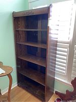 Full view of the tall wooden bookcase showing four shelves and decorative top panel.