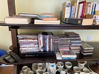 Overview of shelving unit showing Blu-ray player, stacks of DVDs, CDs, audio cassettes, and books above and below.