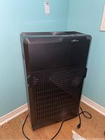 Front view of large black electronic air purifier with cord and casters visible.