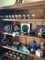 Shelf of various glassware, cat figurines, barometer, steins, and other decorative items