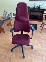 Front view of maroon high-back office chair with attached adjustable cushion and black armrests on wooden floor.