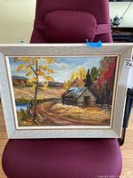 Full view of framed acrylic painting of rural autumn landscape with cabin, tree, dirt road and hills.