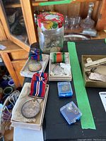 Photo of three military medals in boxes beside a jar with mixed coins on black surface.