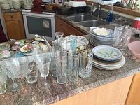 Overview of mixed glassware and porcelain plates stacked on a kitchen counter.