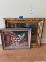 Two framed artworks leaning against wall, showing ornate gold frame print and smaller painting with rural horses scene