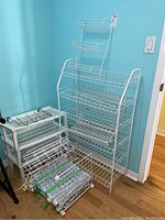 Overall image showing multiple white wire shoe racks, modular storage racks, and resin shelves grouped against a blue wall.