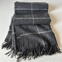 Charcoal colored throw blanket with white stripes displayed folded with fringed ends visible