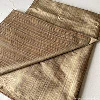 Folded yardage of harvest golden tone striped silk upholstery fabric showing sheen and texture