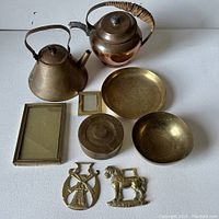 All items in lot shown together on white surface, including brass and copper teapots, horse brasses, picture frames, lidded container, and dishes.
