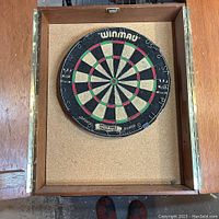 Open wooden dart board cabinet interior showing cork backing and mounted Winmau dart board inside.