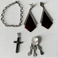 Photo showing the sterling silver bracelet, pair of Art Deco earrings with dark agate center and silver trim, onyx cross pendant, and mother of pearl pendant with dangling pieces.