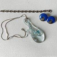 Single image showing sterling silver marina anchor bracelet with a lobster clasp, handmade clear glass pendant with an artistic anchor inside hanging from a fine silver chain, and a pair of blue circular earrings with silver-tone fan design.