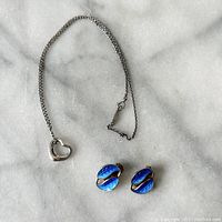 Photo showing the silver heart open pendant necklace and blue guilloche enamel leaf earrings on marble surface.