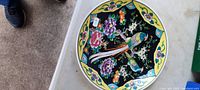 Top view of 12-inch plate showing the full bird and floral colored design on black background with yellow rim featuring floral accents.