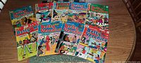 Top view showing 12 vintage Betty and Veronica comic books spread on a wooden table, colorful covers with classic comic illustrations visible.