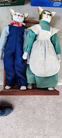 Full view of two cat dolls standing on wooden board, showing porcelain heads and hands with folk art style clothing
