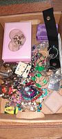 Top view of open box containing assorted colorful beaded necklaces, green necklace, metal chains, pins, earrings, vintage and modern pieces including small jewelry boxes and pouches.