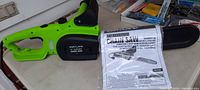 Green Portland 14 inch electric chainsaw with black blade cover and manual placed on table.