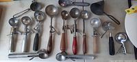 Full overview of the lot showing 15 different antique and vintage ice cream scoops with varied wooden handles and metal bowls.