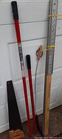 Lot of woodworking tools: two brace bars, large wooden ruler, metal ruler, wooden hand saw, and wooden brace handle with drill bit, all propped vertically against a white door.