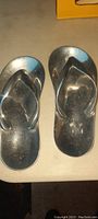 Pair of shiny metal flip flops viewed from the top, showing the reflective finish and strap design.