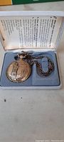 Pocket watch with embossed cover, chain attached, in original box with instruction paper.