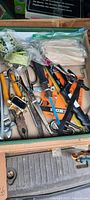 Box of assorted hand tools including pliers, screwdrivers, scissors, and other small tools lying inside a cardboard container.