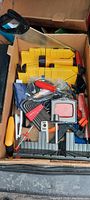 Box filled with assorted woodworking and hand tools including a yellow plastic miter box and saw, various clamps, Allen wrench set, and other small tools.