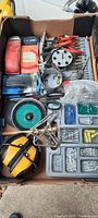 Top view of box showing pliers, drill bit holder, trays of hardware, sanding discs, scissors, hearing protection earmuffs, and tape measure