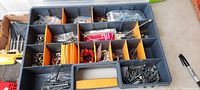 Top view of compartmentalized plastic storage box with various types of screws, nails, washers, and electrical connectors separated in orange dividers