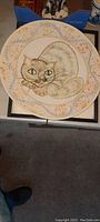 Photo showing front view of the ceramic plate with cat illustration and decorative border.