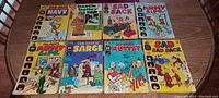 Group photo of 10 vintage comic books on wooden table showing front covers including Sad Sack, Sad Sack and Sarge, Army Life, Muttsy, Beetle Bailey