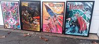 Four framed Marvel posters leaning against a wall outdoors showing detailed comic art and characters.