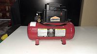 Front view of small red air compressor with Jobmate branding, black motor unit on top and warning labels on tank.