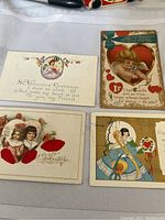 All four antique Valentines Day postcards arranged on cloth surface.