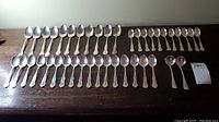 Top-down view of all 41 Birks silver-plated spoons arranged in rows by type on a wooden surface.