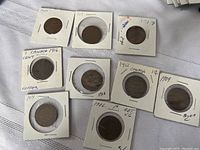 Nine Canadian large pennies in cardboard holders with hand-written labels of dates and condition notes.