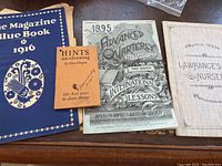 Four antique booklets and magazines shown together on a wooden surface, showing titles and spines
