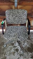 Front view showing zebra pattern upholstery on seat and backrest, black armrests, metal base with five caster wheels