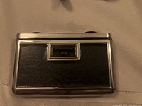 Front view of closed opera glasses in chrome metal casing with black faux leather covering.
