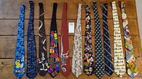 Full view of all eleven ties laid out flat on wood surface showing a variety of character and theme prints.