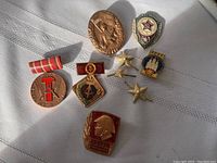 All pins and buttons arranged on white fabric, showing full lot including 4 East German pins and 2 USSR buttons with some varied shapes and colors including gold, red, and bronze tones.