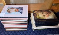 Photo showing two stacks of art books with portrait images on covers and gold embossed titles on spines.
