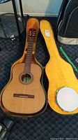 Full view of the acoustic guitar inside yellow-lined black hard case with tambourine inside case