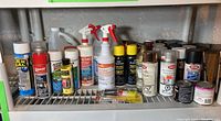 Multiple cans of spray paint, sealants, adhesives, and other chemical sprays arranged on a wire shelf.