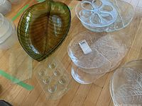 Top view of assorted glass leaf-shaped bowls and clear serving plates with leaf patterns and indents, arranged on floor.
