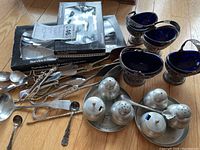 Overview of the pewter condiment sets, blue glass bowls, and serving utensils arranged on a wooden floor.