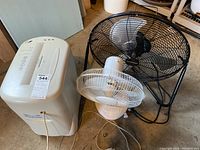 Photo showing all three items: a beige Royal VF1000 shredder, a black metal cage fan, and a white plastic cage fan side by side on floor.