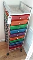 View of the full tall metal storage rack with 10 colorful plastic drawers on black wheels on wood floor.