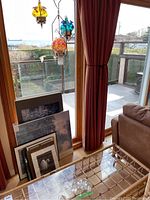 Partial view of small paintings or prints piled near the window and the glass table holding the sun catchers, indicating additional background context.